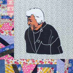 Leah Chase smiling in a black chef coat.